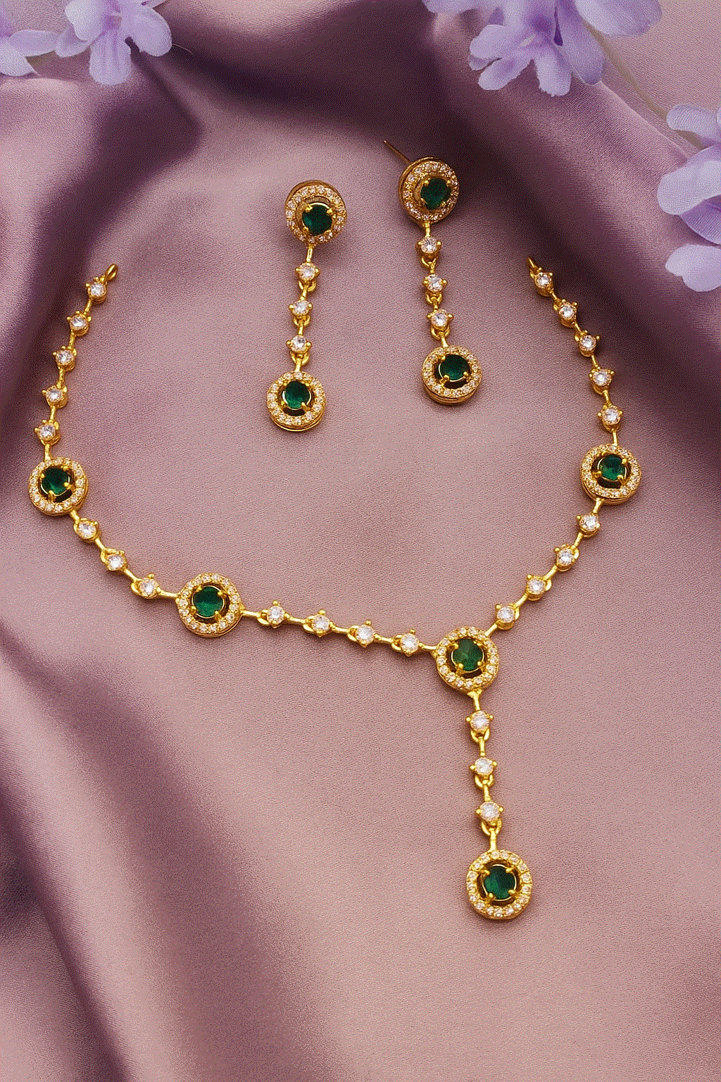 Gold plated bridal necklace and dangler earrings set with emerald green CZ diamonds on purple fabric