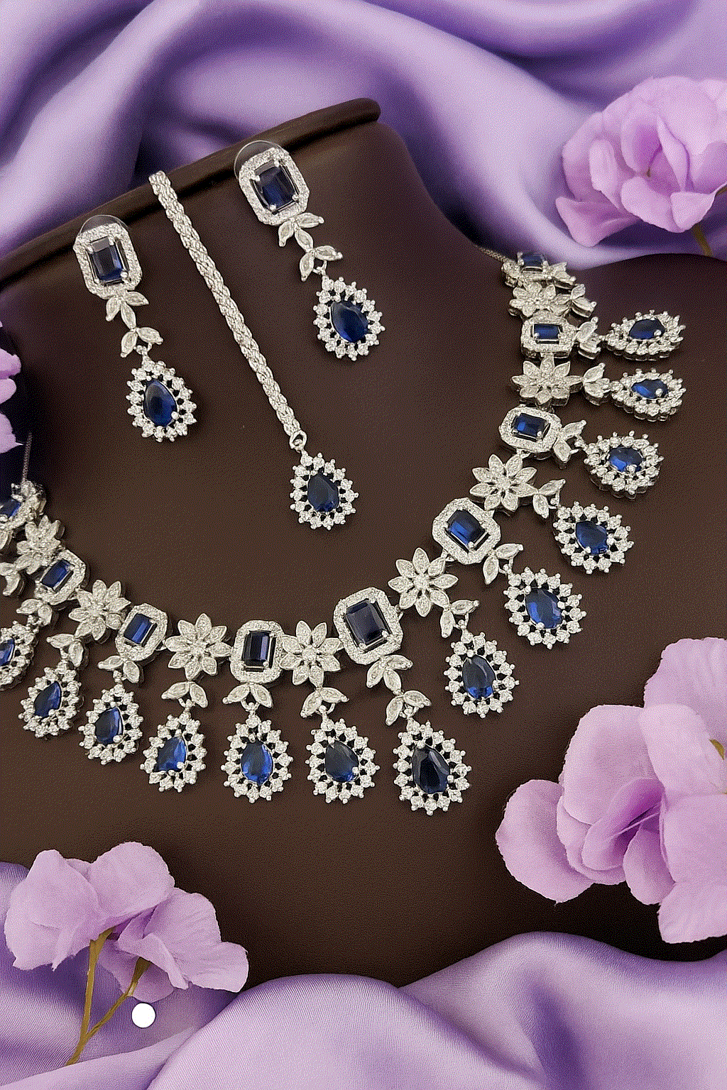 Regal Deep Sapphire bridal jewelry set with blue CZ diamonds, necklace, earrings, and Maang Tikka on purple fabric background