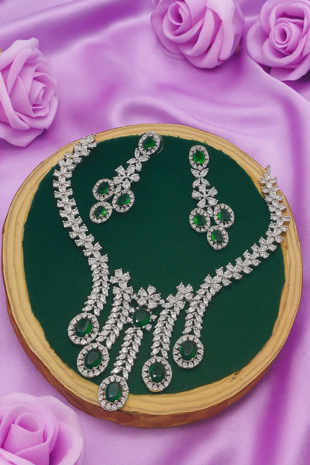 Luxury bridal silver-plated necklace set with emerald green CZ and matching earrings on green display with purple rose decor