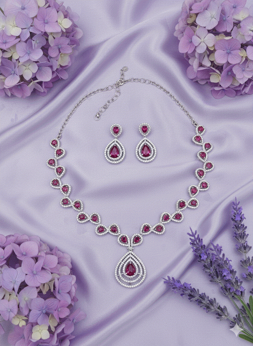 Regal intimate jewelry set with ruby red cubic zirconia necklace and matching earrings on purple satin background with flowers