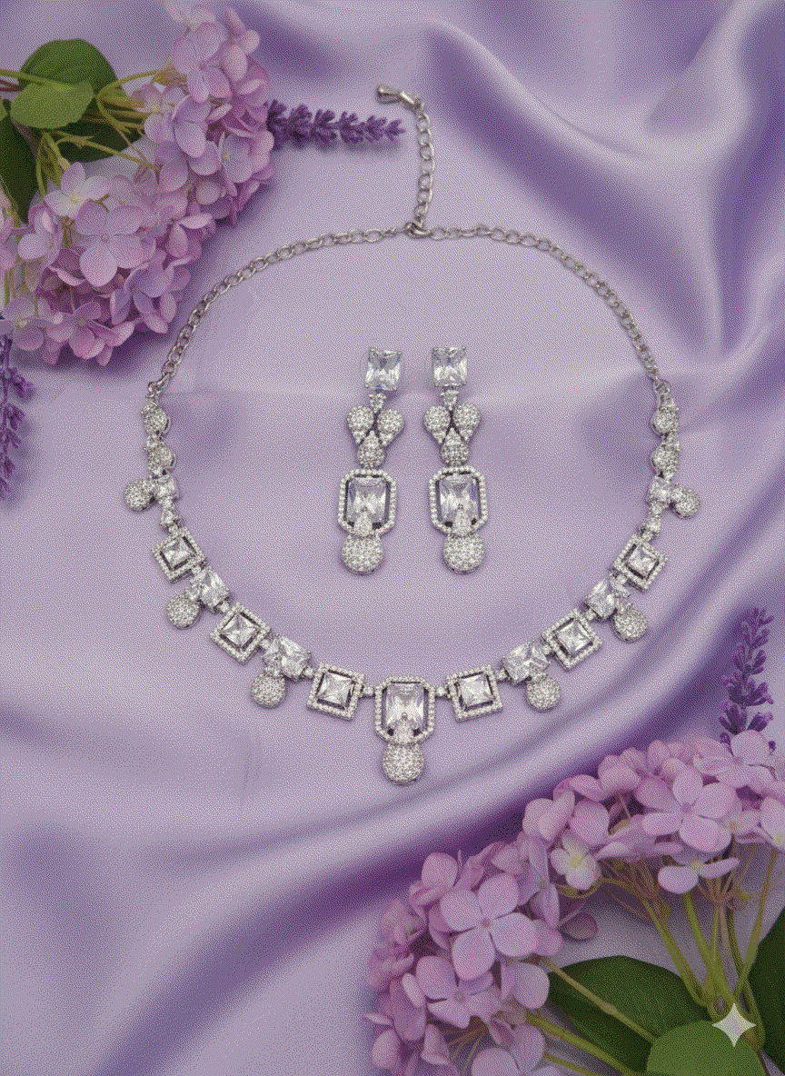 Intimate Jewelry necklace set with geometric square-cut CZ and pavé balls in rhodium-plated finish on lavender fabric with purple flowers