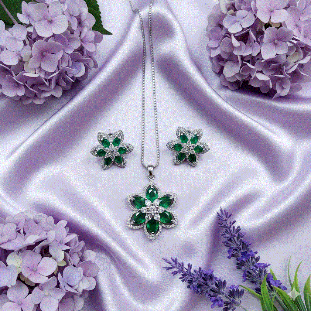 Elegant intimate jewelry set with emerald green marquise-cut CZ floral pendant and matching earrings on rhodium plated chain displayed on lavender silk with purple flowers.