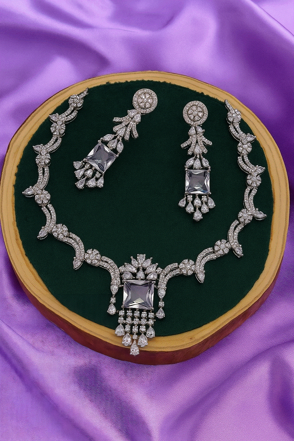 Regal CZ Diamond Jewelry set with rhodium-plated bridal necklace and long dangler earrings on purple satin background