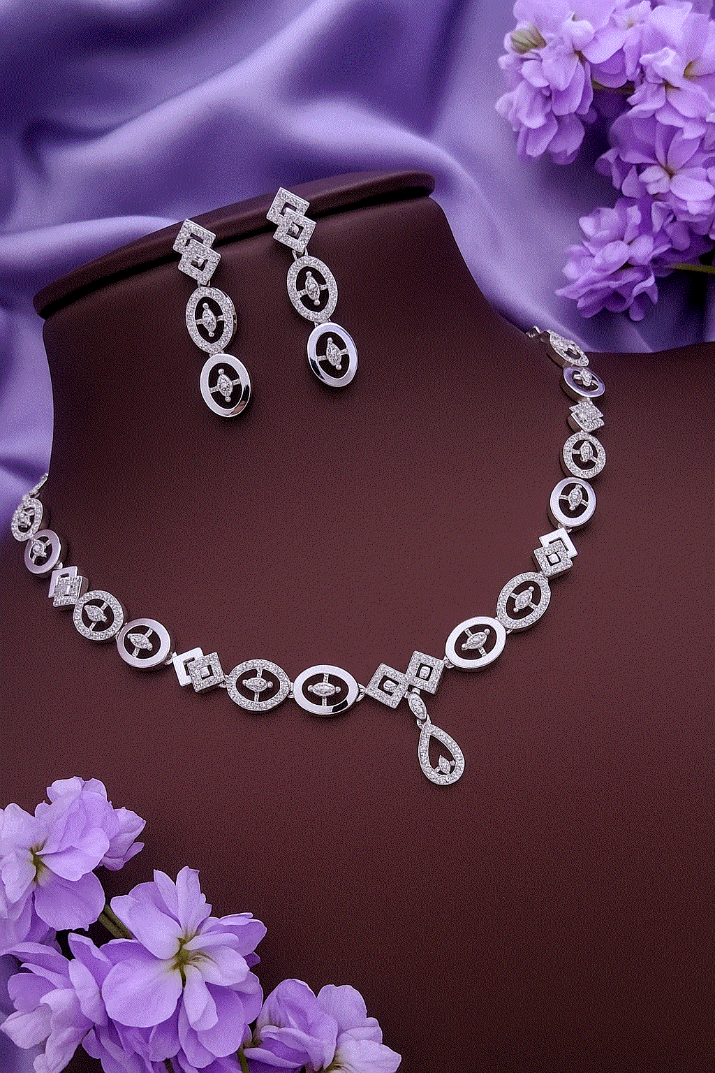 Geometric CZ diamond necklace and dangler earrings set in silver tone with sparkling micro-pave stones on purple background