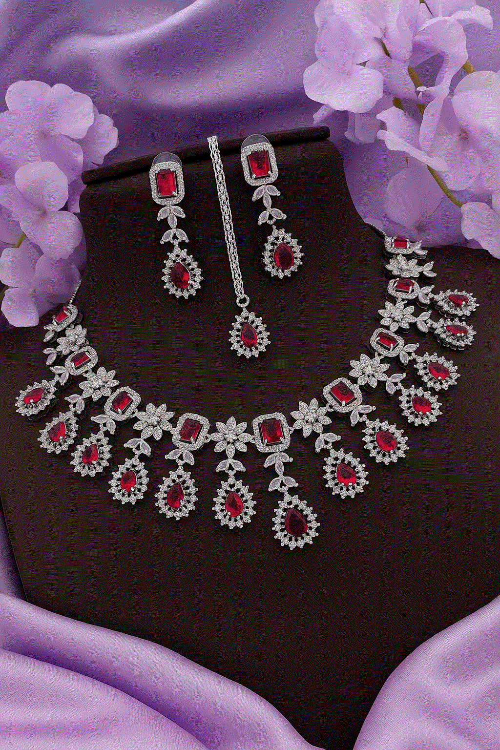 Regal Ruby Red CZ diamond bridal necklace, earrings, and maang tikka jewelry set on purple fabric background