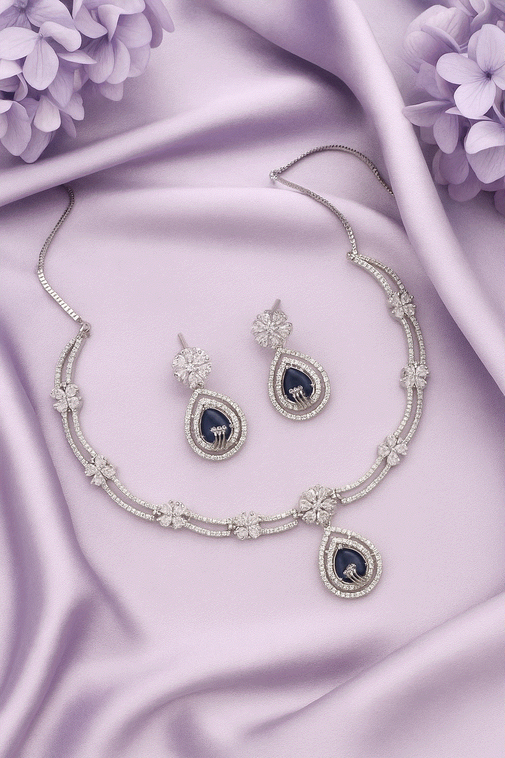Intimate Jewelry Sapphire Blue CZ floral drop necklace and earrings set with rhodium plating on lavender fabric background