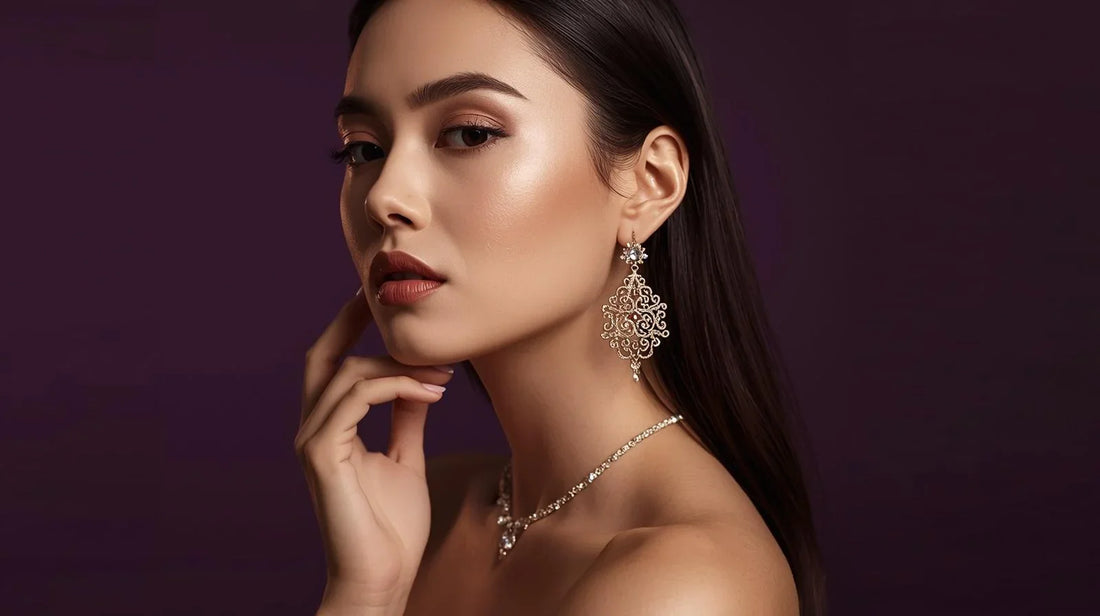 Elegant woman wearing intricate gold earrings and a sparkling necklace by Miraasi Jewels against a dark background