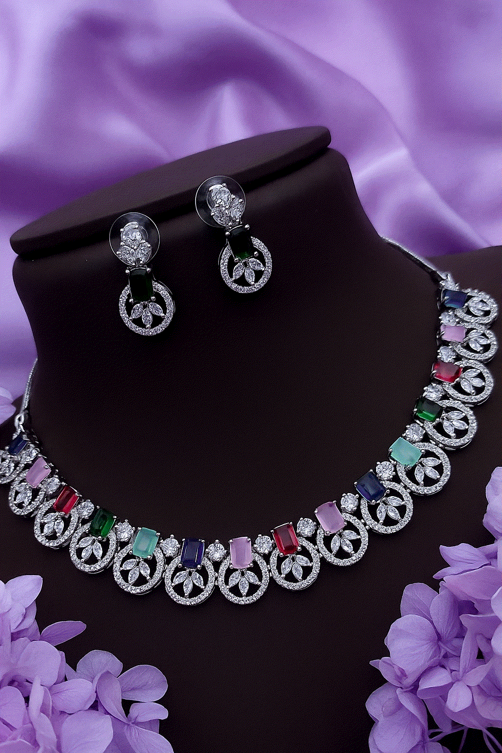 Vibrant multi-color CZ diamond necklace and stud earrings set with silver-toned floral design on black display bust against purple satin background