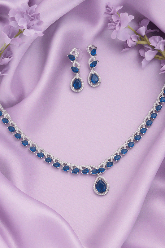 Dazzling sapphire blue CZ diamond necklace and drop earrings set with white gold tone on purple satin background