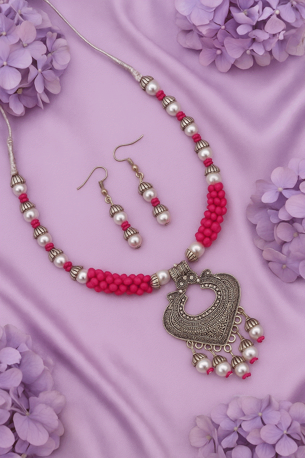 Vibrant pink bead and pearl oxidized silver tone necklace with matching drop earrings on purple silk background with flowers
