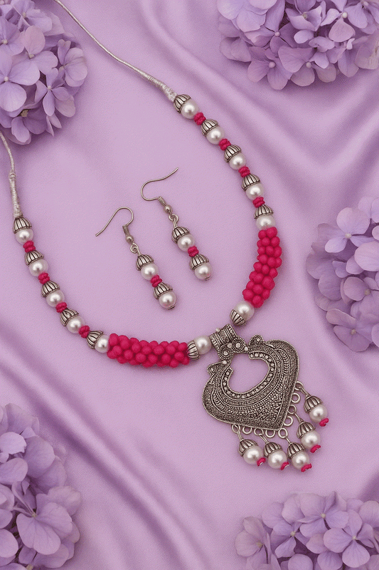 Vibrant pink bead and pearl oxidized silver tone necklace with matching drop earrings on purple silk background with flowers