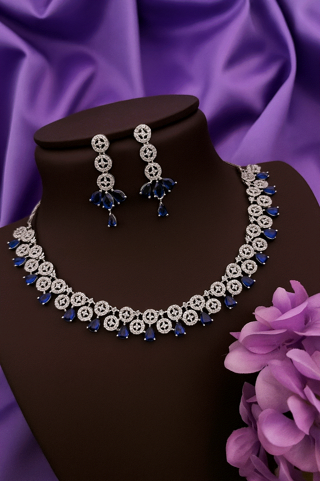 Dazzling Sapphire Blue Drop CZ Choker Set with silver-toned bridal necklace and matching dangling earrings on black display against purple fabric background