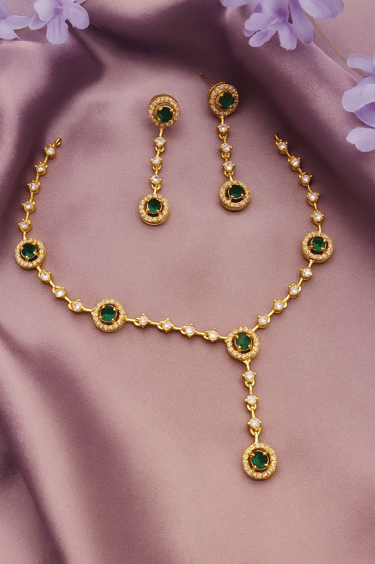 Gold plated bridal necklace and dangler earrings set with emerald green CZ diamonds on purple fabric