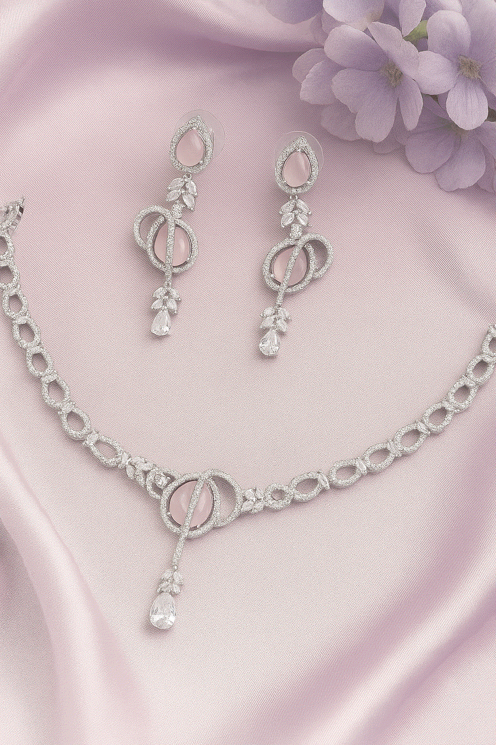 Luxury CZ Intimate Jewelry Set with rose quartz pink gemstone necklace and rhodium-plated earrings on pink fabric background