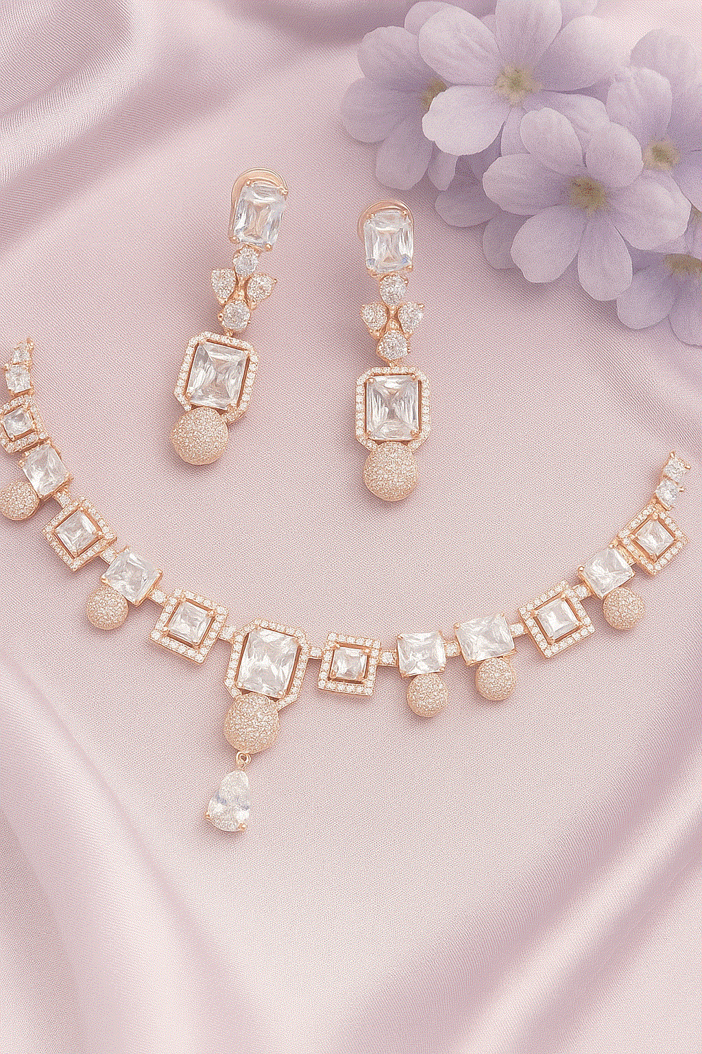 Luxury CZ Intimate Jewelry Set with rose gold geometric bridal necklace and diamond look earrings on pink satin background