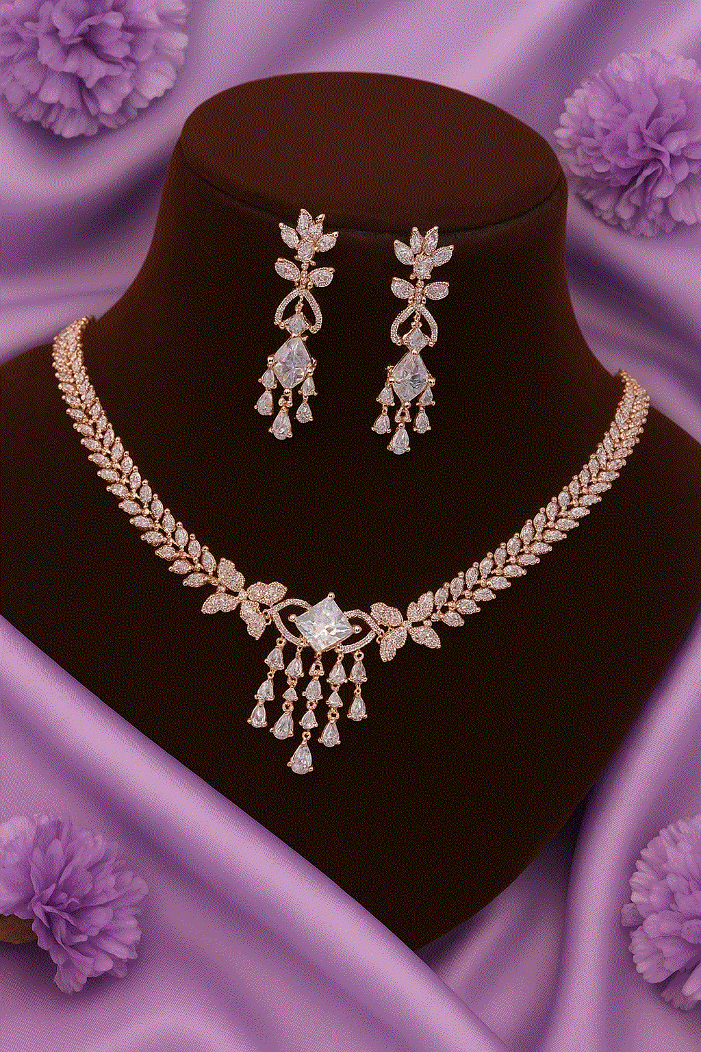 Luxury CZ intimate jewelry set with rose gold leaf vine bridal necklace and diamond look chandelier earrings on a display bust with purple floral background