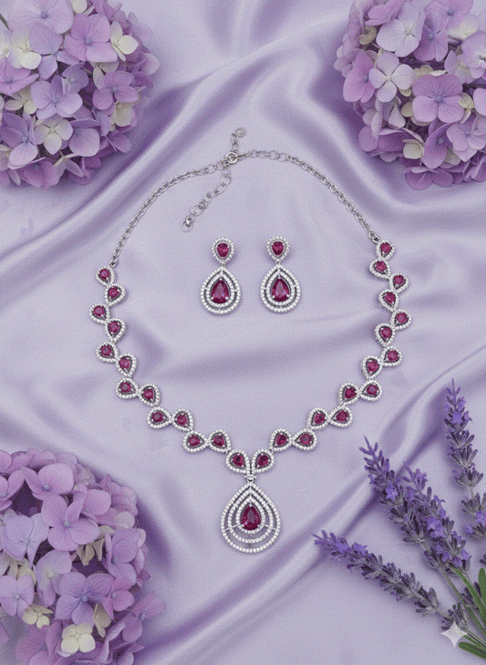 Regal intimate jewelry set with ruby red cubic zirconia necklace and matching earrings on purple satin background with flowers
