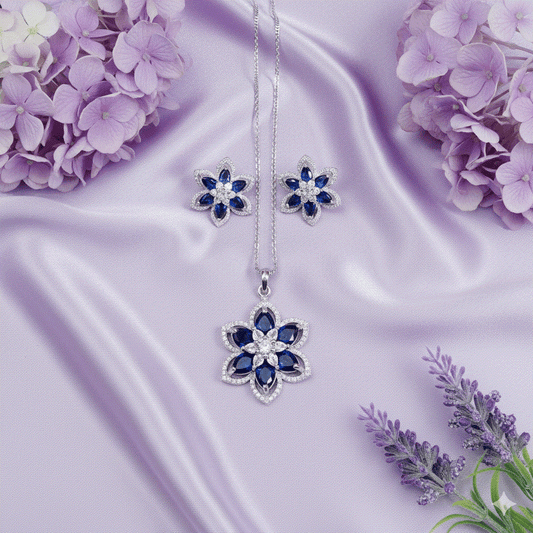 Elegant intimate jewelry sapphire blue floral pendant and stud earring set with rhodium plating on lavender satin background
