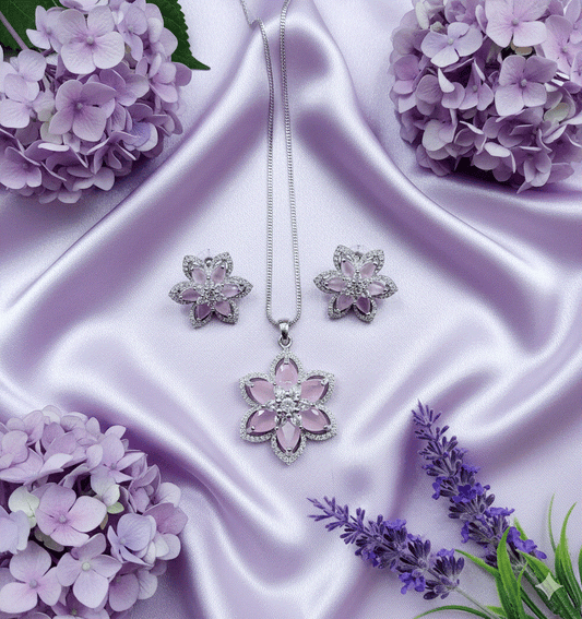 Intimate Jewelry clear CZ floral pendant and earrings set on rhodium plated chain displayed on lavender satin with purple flowers