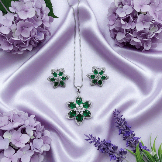 Elegant intimate jewelry set with emerald green marquise-cut CZ floral pendant and matching earrings on rhodium plated chain displayed on lavender silk with purple flowers.