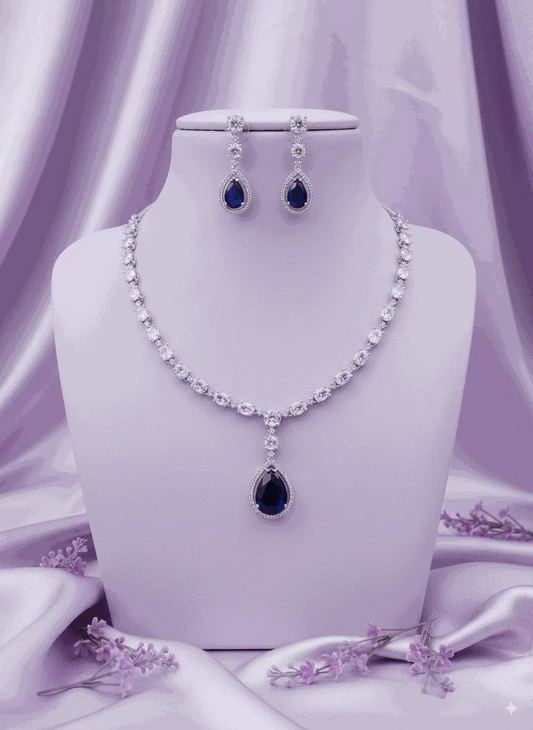 Royal blue sapphire CZ diamond necklace and drop earrings set with silver-toned plating on purple fabric background