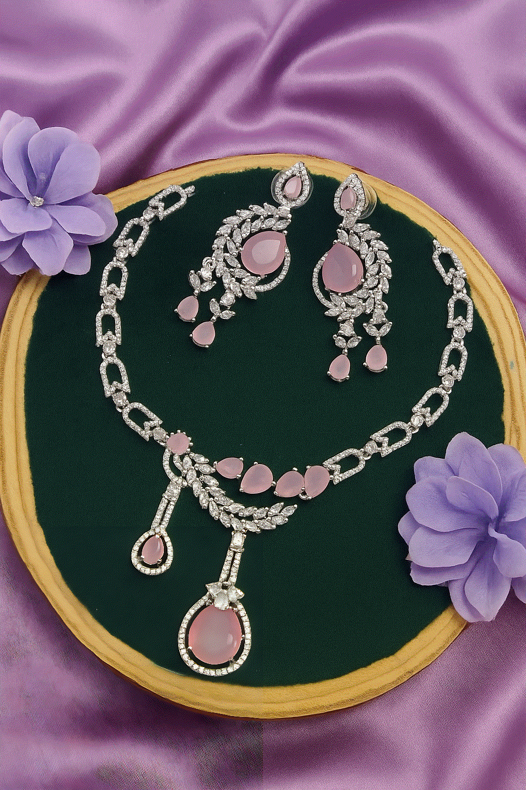 Luxury CZ diamond jewelry set with rose gold necklace and dangler earrings on purple fabric background
