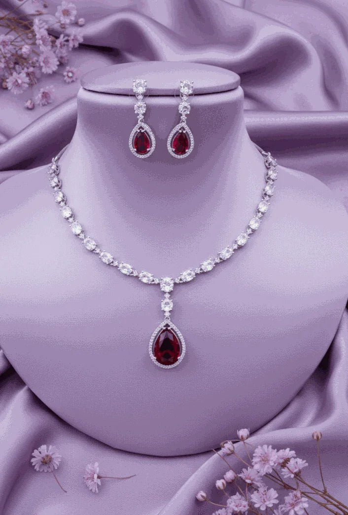 Passionate Ruby Red pear-shaped CZ drop necklace and earrings set in silver-toned with white CZ stones on purple fabric background
