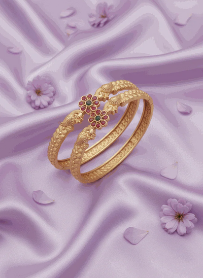 Matte gold plated traditional floral jewelry bangles with ruby and emerald stones on purple silk background