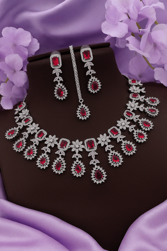 Regal Ruby Red CZ diamond bridal necklace, earrings, and maang tikka jewelry set on purple fabric background