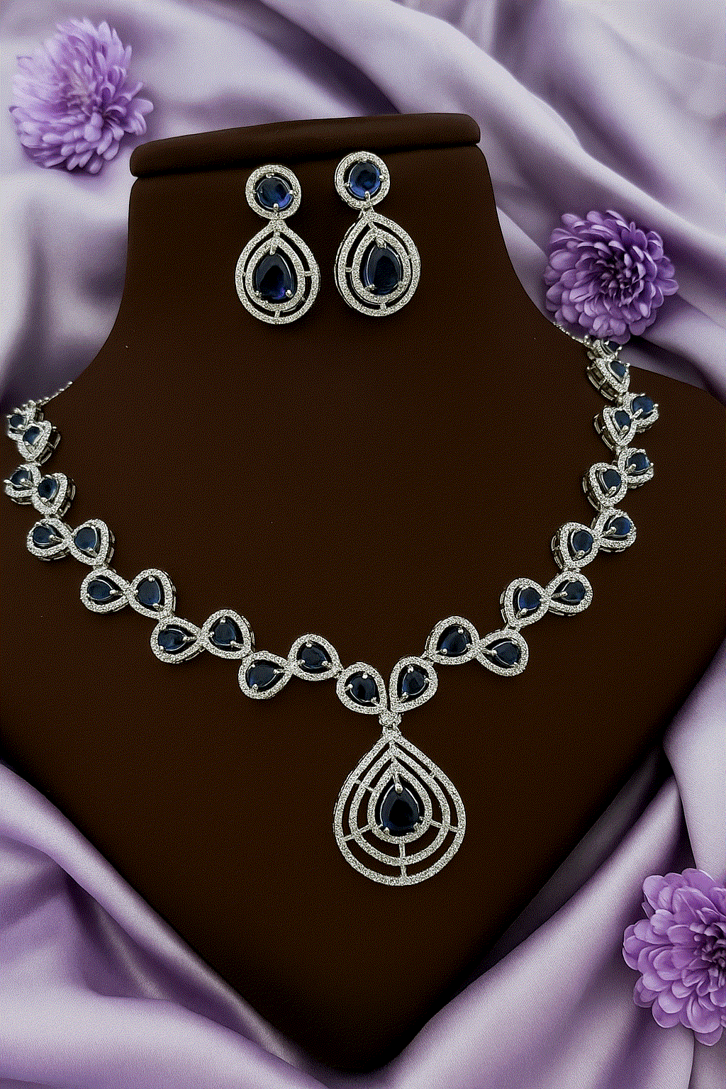 Luxury Deep Sapphire CZ diamond white gold tone bridal necklace and drop earrings set on purple fabric background