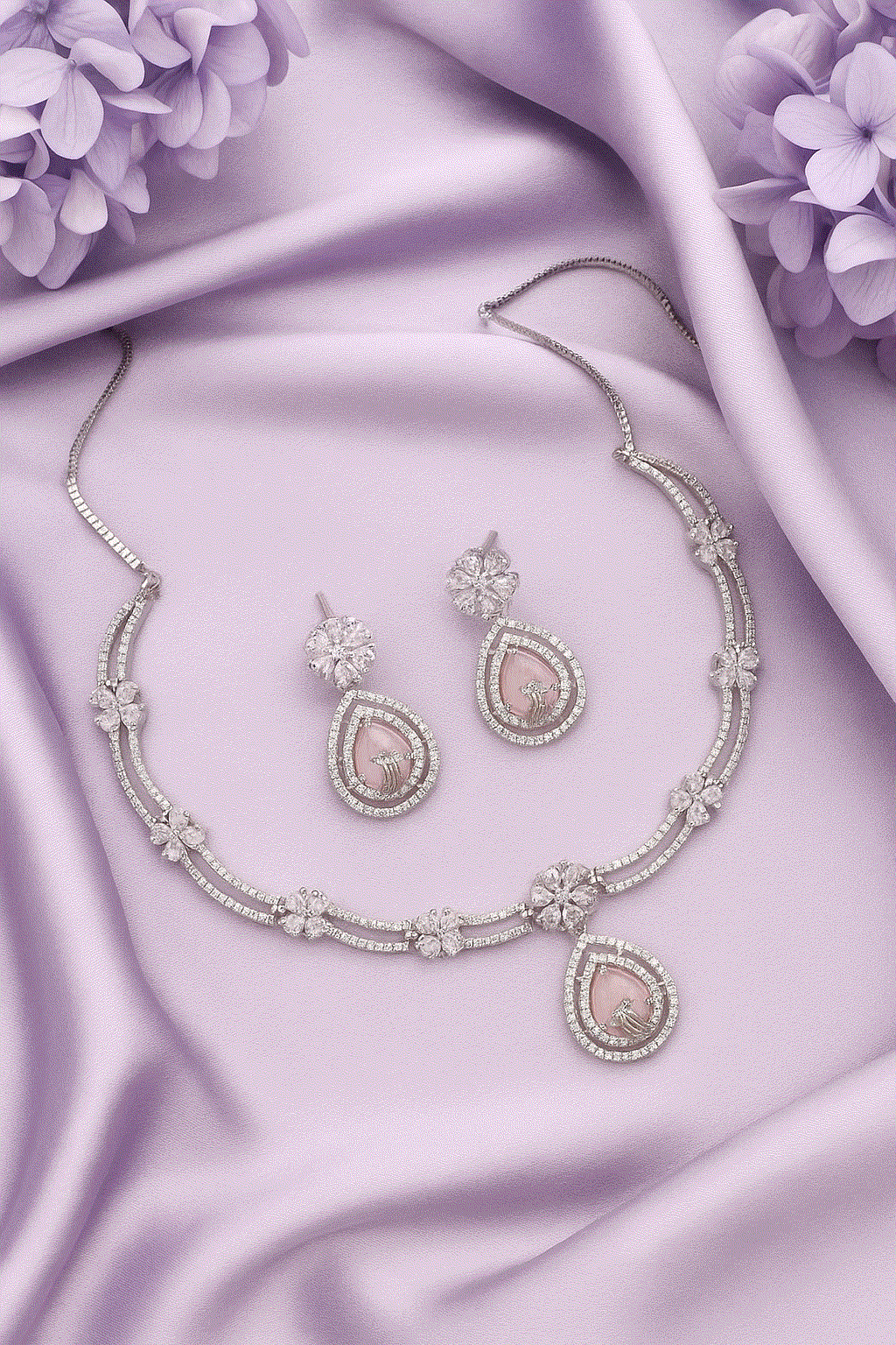 Elegant Intimate Jewelry pink CZ floral drop necklace and earrings set with rhodium plating on lavender silk background